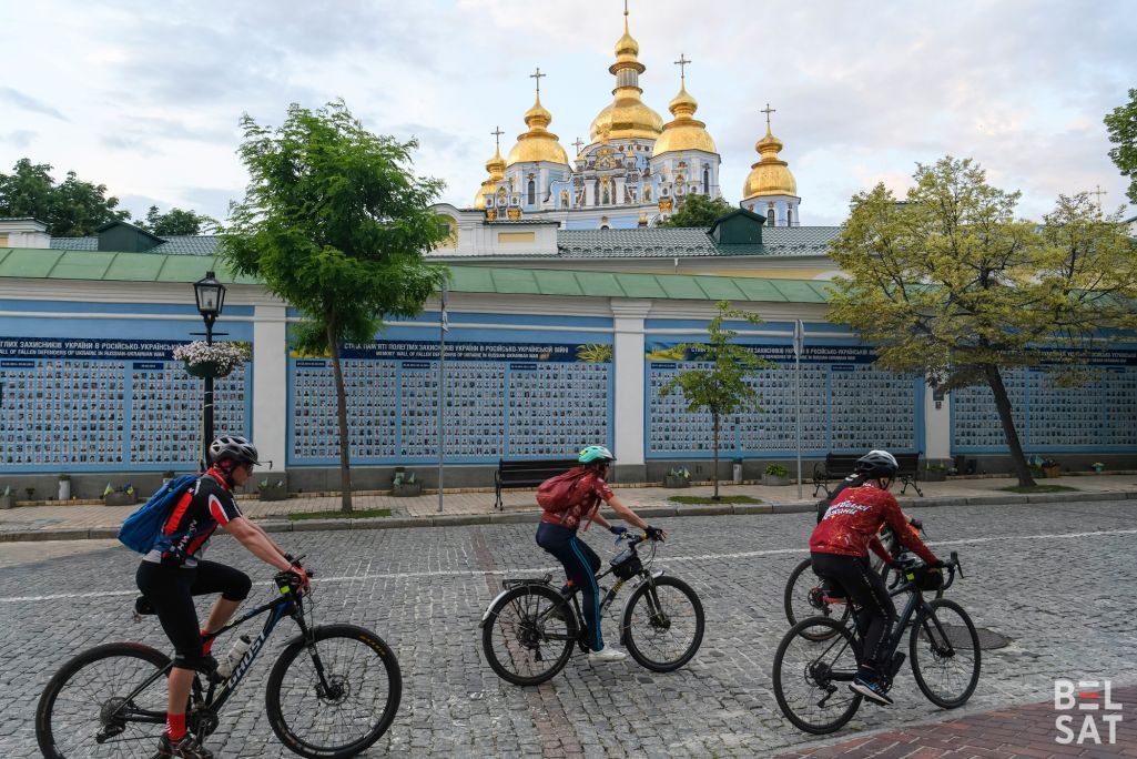 Раварысты праязджаюць міма Сцяны памяці з фотаздымкамі ўкраінскіх вайскоўцаў, якія загінулі ў вайне з расейскімі акупантамі з 2014 года. Кіеў, Украіна. 28 траўня 2024 года. (Фота: Уладзіслаў Максіменка / Белсат)
