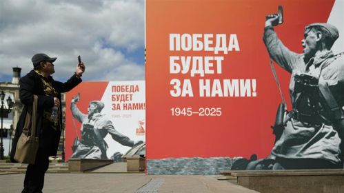 Мужчина фотографирует плакат с фотографией советского офицера во время Второй мировой войны накануне Дня Победы