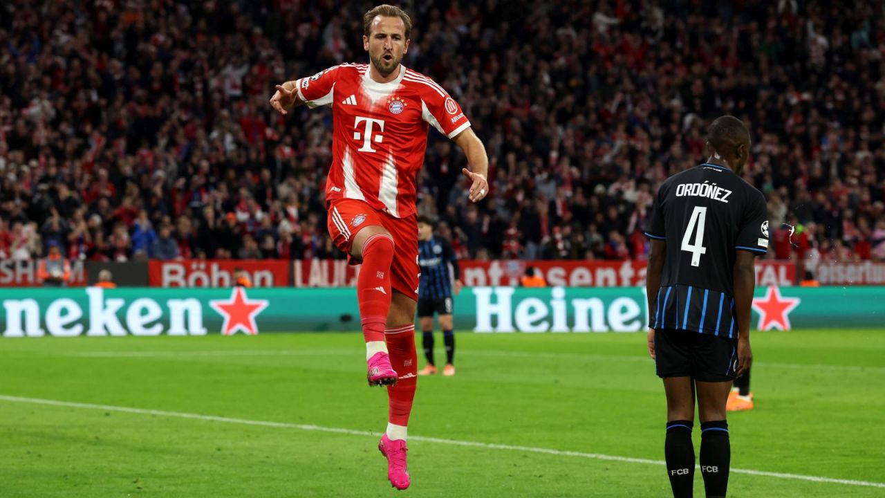 Piłkarz Bayernu Monachium Harry Kane świętuje zdobycie bramki w meczu Ligi Mistrzów przeciwko Club Brugge, skacząc w geście radości na tle kibiców.