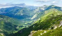 Widok z Kasprowego Wierchu na polskie Tatry. Krajobraz gór oraz doliny pokrytych zielenią. 