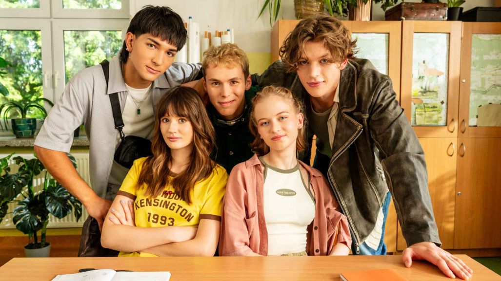 „Piep*zyć Mickiewicza 2” oglądaj w TVP VOD od 13 listopada. W klasie szkolnej pięcioro uczniów siedzi i stoi przy ławce. Za nimi znajdują się szafki i rośliny doniczkowe, a na biurku leżą zeszyty.